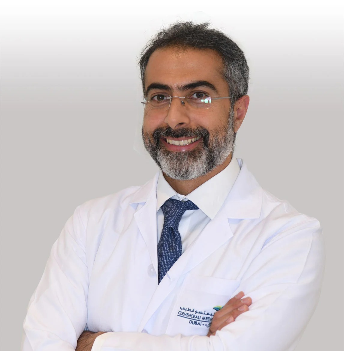 A man in a white doctor's coat, smiling and standing with arms crossed